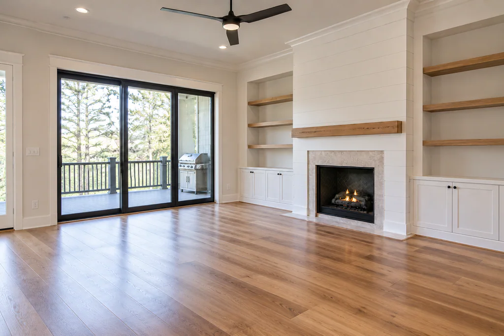 Empty living room with a fireplace, built-in shelves, wood flooring, and sliding doors to a deck.