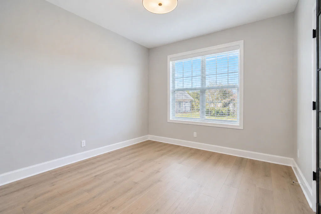 Home office before virtual staging: light room with a large window and blue-sky view, shown empty.